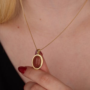 May include: A gold chain necklace with a pendant featuring a round, reddish-brown stone set in a gold frame.