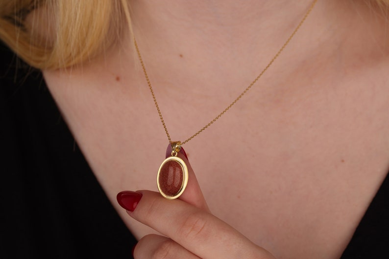 May include: A gold chain necklace with a pendant featuring a round, reddish-brown stone set in a gold frame.
