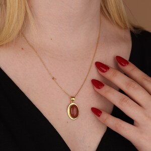 May include: A gold chain necklace with a pendant featuring a reddish-brown oval stone set in a gold frame.