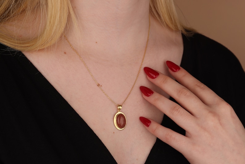 May include: A gold chain necklace with a pendant featuring a reddish-brown oval stone set in a gold frame.