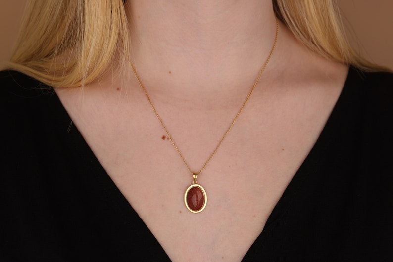 May include: A gold chain necklace with a brown oval pendant.