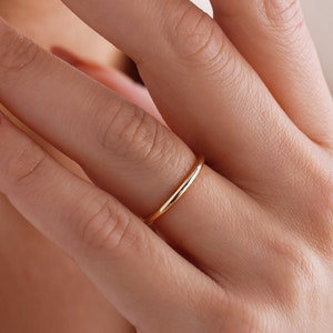 May include: A close-up of a hand with nude nail polish and gold glitter accents, wearing a thin gold band ring.