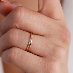 May include: A close-up of a hand wearing a gold, double-band ring. The ring is simple and elegant, with a delicate, intertwined design.