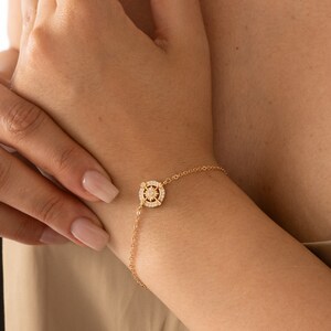 May include: A gold chain bracelet with a small, round pendant featuring a starburst design with clear crystals.