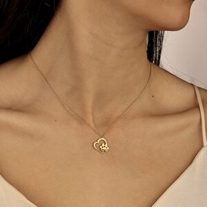 May include: A gold necklace with a heart pendant featuring a paw print inside. The necklace is on a model's neck.
