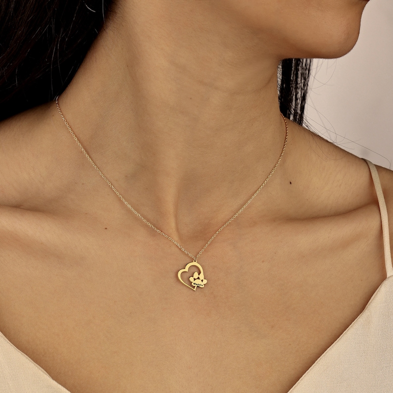 May include: A gold necklace with a heart pendant featuring a paw print inside. The necklace is on a model's neck.