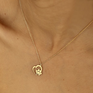 May include: A gold necklace with a heart pendant featuring a paw print inside. The pendant is on a delicate chain.