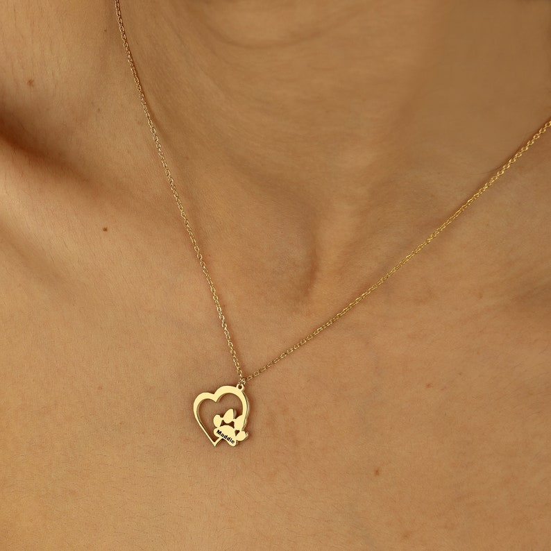 May include: A gold necklace with a heart pendant featuring a paw print inside. The pendant is on a delicate chain.