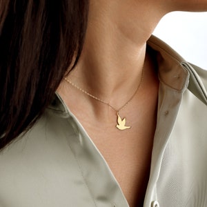 K&ouml;nnte beinhalten: Eine goldene Kettenkette mit einem zarten Taubenanh&auml;nger. Die Taube ist ein Symbol f&uuml;r Frieden und Hoffnung.