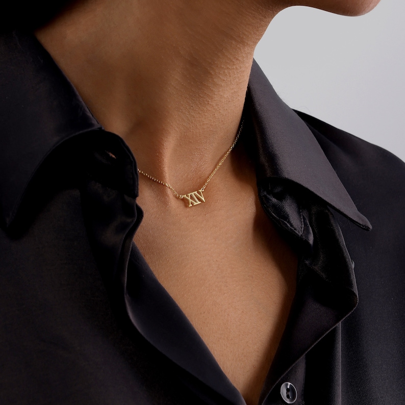 May include: A gold necklace with a Roman numeral pendant that reads "XXV".
