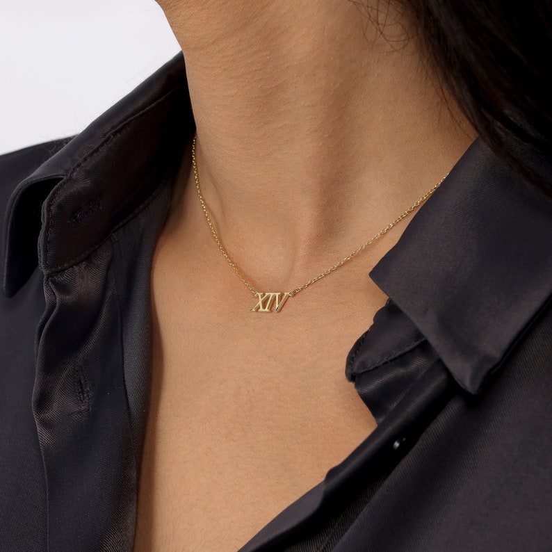 May include: A gold necklace with a Roman numeral pendant that reads "XIV".