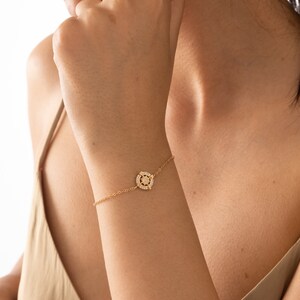 May include: A gold bracelet with a small, round charm featuring a starburst design with clear crystals.