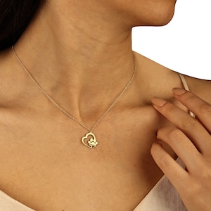 May include: A gold necklace with a heart pendant featuring a paw print inside. The necklace is on a model's neck.