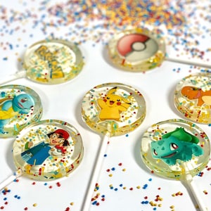 May include: Six round lollipops with different Pokemon characters on them. The lollipops are clear and have colorful sprinkles on them. The lollipops are on a white surface with colorful sprinkles scattered around them.