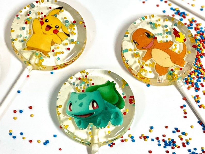 May include: Three round lollipops with colorful sprinkles. Each lollipop features a different Pokemon character: Pikachu, Charmander, and Bulbasaur.