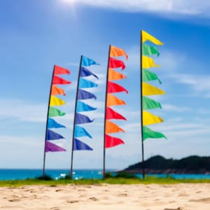 May include: Four colourful pennant flags with multiple triangular sections in a rainbow pattern, hanging from poles against a blue sky and beach background.