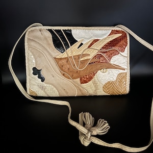 May include: A white leather crossbody bag with a flap closure. The bag is made of different types of leather, including snakeskin, ostrich, and lizard. The bag has a long strap with a tassel.
