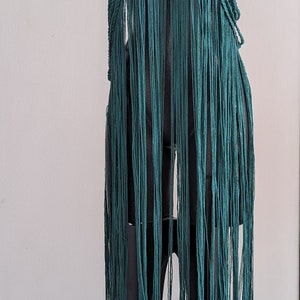 May include: A teal crochet top with fringe and wooden beads. The top is on a black mannequin.