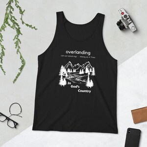 May include: Black tank top with a white graphic design of a mountain landscape with trees and a river. The text "overlanding" is at the top of the design, with the definition "oh-ver-luhnd-ing/ Hiking on 4 Tires" below it. The text "In God's Country" is at the bottom of the design.