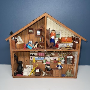 May include: A detailed miniature wooden house with two stories, filled with tiny figurines and furniture. The house has a brown exterior and a blue background. The interior includes a stove, shelves, and a US Mail box.