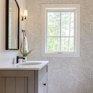 May include: A bathroom vanity with a white countertop and a gray cabinet. A black faucet and a round sink are visible. A mirror with a black frame hangs on the wall. The wallpaper has a gray leaf pattern. A window with a view of trees is on the right.