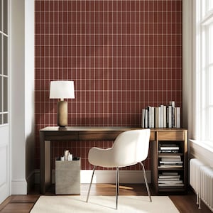 May include: A home office with a dark wood desk, a white chair, and a lamp with a beige base and white shade. The wall is a deep red with a grid pattern. Bookshelves and a wastebasket are also visible.