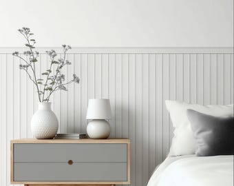 May include: A modern bedroom scene featuring a gray nightstand with two drawers and wooden legs. A white lamp and a textured white vase with floral branches sit atop the nightstand. A bed with white bedding and pillows is in the background.