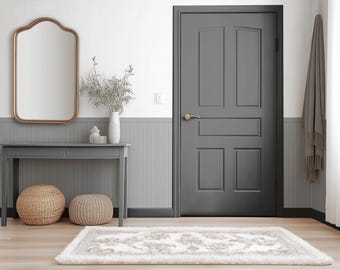 May include: A gray entryway with a decorative mirror, console table, and a gray door. A woven basket and a round ottoman sit beneath the table. A patterned rug lies on the wooden floor. A gray scarf hangs on the wall.