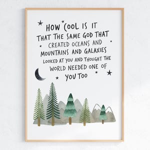 May include: A framed art print with a light wood frame. The print features a whimsical watercolor illustration of trees and mountains beneath the text: "HOW COOL IS IT THAT THE SAME GOD THAT CREATED OCEANS AND MOUNTAINS AND GALAXIES LOOKED AT YOU AND THOUGHT THE WORLD NEEDED ONE OF YOU TOO."