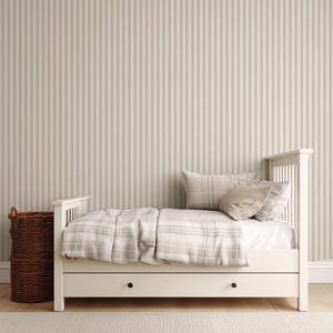 May include: A white twin bed with a plaid comforter and pillows. The bed has a drawer underneath and is set against a striped beige and white wall. A woven basket sits to the left of the bed.