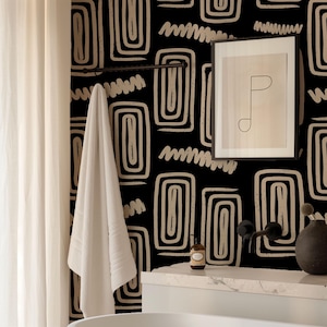 May include: A bathroom scene featuring a black and beige patterned wallpaper. A white towel hangs on a dark metal bar. A framed abstract art print and a dark vase are on a white countertop. A bottle of soap sits on the counter.