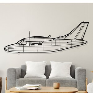 May include: A black metal wireframe airplane wall decor hanging on a white wall above a gray couch and a wooden coffee table. A white lamp is in the background.