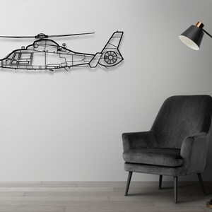 Peut inclure: Une silhouette noire en m&eacute;tal d'un h&eacute;licopt&egrave;re mont&eacute;e sur un mur blanc. Un fauteuil noir avec un rev&ecirc;tement en tissu gris est plac&eacute; devant un lampadaire noir avec un abat-jour blanc.