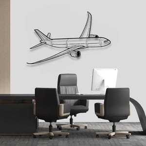 Puede incluir: Una pieza de arte mural de avión de metal negro. El avión está representado en un dibujo lineal detallado, con alas, cola y motor visibles. La obra de arte está montada en una pared gris claro sobre un escritorio y sillas de oficina modernos.