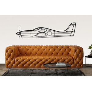 May include: Black metal airplane wall decor with a simple outline design. The airplane is hanging above a brown leather sofa and a black coffee table.