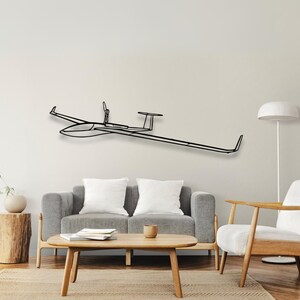 Può includere: Un'opera d'arte da parete in metallo nero raffigurante un aliante. L'aliante è raffigurato in uno stile minimalista, con un design elegante e lineare. L'opera d'arte è montata su una parete di colore neutro, sopra un divano grigio e un tavolino di legno.