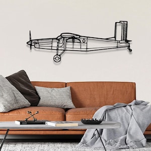 May include: Black metal wall art of a single-engine airplane with a propeller. The airplane is mounted on a white wall above a brown leather couch with gray throw pillows and a gray throw blanket.
