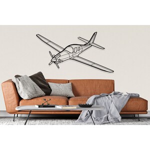 May include: A black metal airplane wall decor with a minimalist design. The airplane is mounted on a white wall above a brown leather couch with gray throw pillows and a gray blanket.
