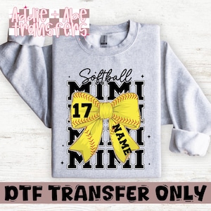 May include: Gray sweatshirt with a black and yellow softball design. The design features a yellow bow with a softball in the center and the text "Softball Mimi" above and below the bow. The number "17" is on the left side of the bow and the word "NAME" is on the right side of the bow.