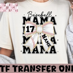 May include: White t-shirt with a black baseball-themed design. The design features a white bow with red stitching and gold accents, with the words "Baseball Mama" and "Name" in black text.