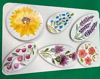May include: Six painted wooden flower shapes, including a sunflower, a bluebell, a lavender, a cherry blossom, a thistle, and a poppy.