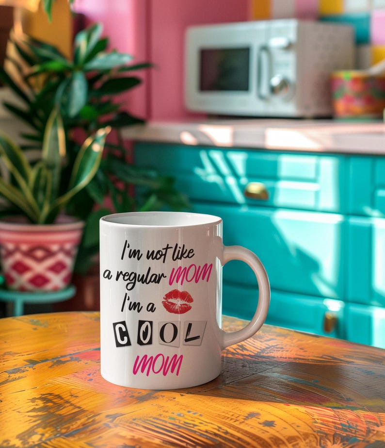 A high-quality white ceramic coffee mug with bold black script that reads "I'm Not Like a Regular Mom, I'm a Cool Mom," sitting on a cozy wooden table with a steaming cup of coffee, making it the perfect funny and thoughtful gift for moms who love caffeine.