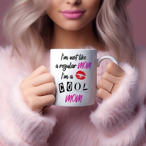Blonde stylish mom in pink sweater holding white coffee mug with the mean girls quote I'm not a regular mom I'm a cool mom.