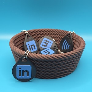 Könnte beinhalten: Eine braune Schnur-Schale gefüllt mit Schlüsselanhängern mit dem LinkedIn-Logo. Die Schlüsselanhänger sind schwarz mit einem blauen LinkedIn-Logo.