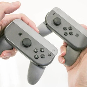 Pode incluir: Dois controladores Joy-Con cinzentos para Nintendo Switch com botões pretos e uma alça cinza e preta.