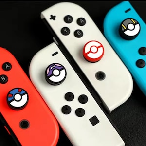 Könnte beinhalten: Nahaufnahme von vier farbenfrohen Gamecontrollern. Die Controller sind rot, weiß und blau, mit schwarzen Knöpfen. Jeder Controller hat ein einzigartiges kreisförmiges Design auf dem Joystick, mit einem rot-weißen Design, einem lila-weißen Design und einem schwarz-gelben Design.