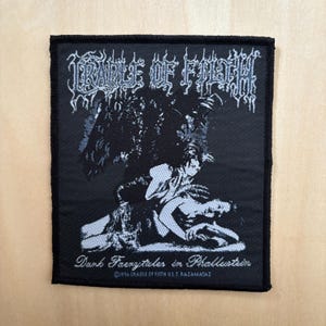 Op de afbeelding: Zwart vierkantige patch met witte gotische tekst "CRADLE OF FILTH". De patch heeft een donkere illustratie en de tekst "Dark Faerytales in Phallustein". Copyright 1996.