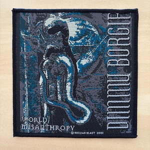 Può includere: Toppa quadrata con bordo blu scuro. Presenta una grafica dettagliata nelle tonalità del blu, grigio e bianco. La toppa ha il testo "DIMMU BORGIR" verticalmente sul lato destro e "WORLD misanthropy" in basso. È presente anche il testo "NUCLEAR BLAST 2003".