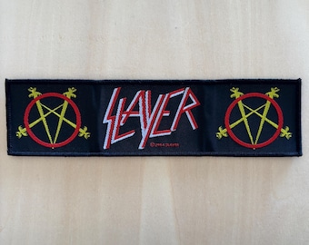 May include: A rectangular black embroidered patch featuring the word Slayer in white and red lettering. On both the left and right sides, there is a yellow pentagram symbol enclosed within a red circle. The text 2004 SLAYER is visible below.