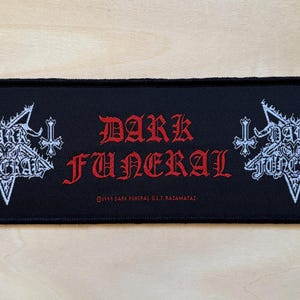 Pode incluir: Um emblema retangular de tecido preto com o texto DARK FUNERAL em letras góticas vermelhas no centro. Em ambos os lados, há um design de pentagrama bordado em branco com cruzes invertidas e o texto DARK FUNERAL dentro de cada estrela.